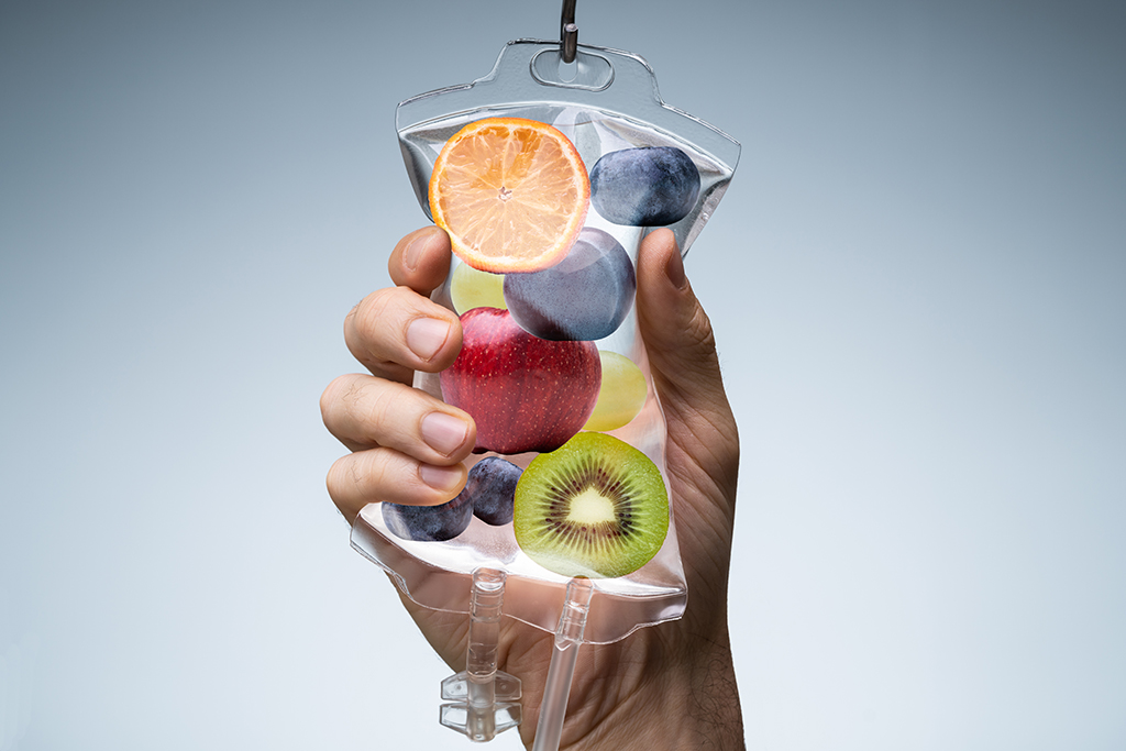 Person's Hand Holding Saline Bag Filled With Various Fruit Slices Against Grey Backdrop